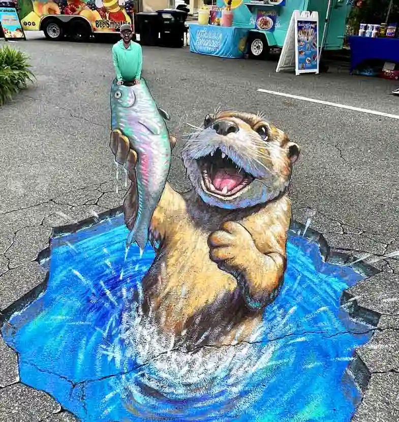 3D chalk art of a hungry otter bursting from the pavement, a 10ft x 20ft street painting by Chris Carlson in Tallahassee, Florida